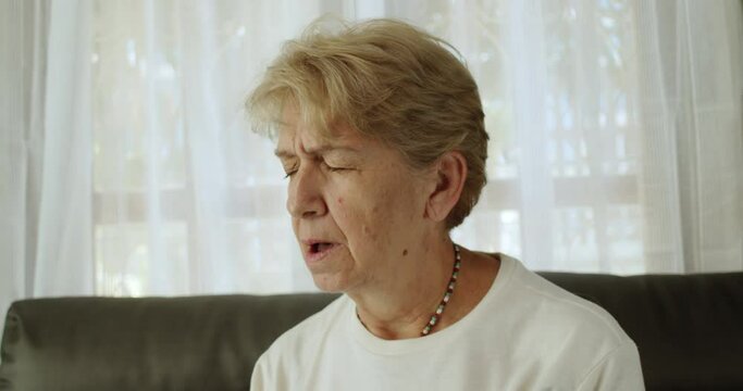 An elderly woman after retirement cut short hair with light brown hair wearing a round neck long a sleeve T-shirt and a necklace feel tired and lethargic until yawning at her home alone.