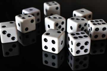 A close up image of several white dice on a black reflective table top. 