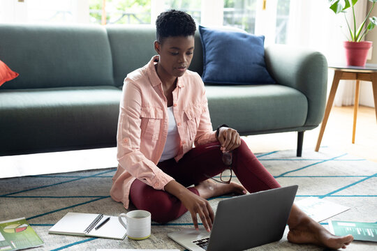 African american woman sitting on floor using laptop drinking coffee working from home