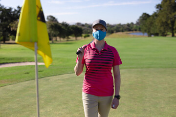 Portrait of caucasian woman wearing face mask holding club on golf course