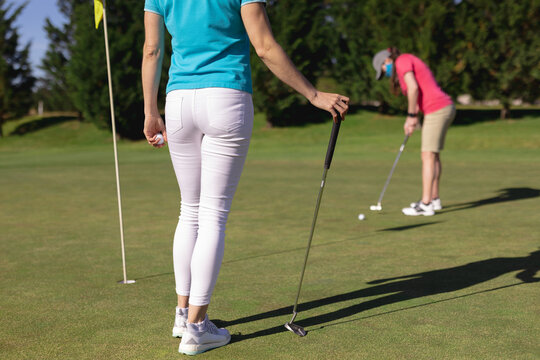 Two caucasian women wearing face masks playing golf one putting to the hole - Powered by Adobe