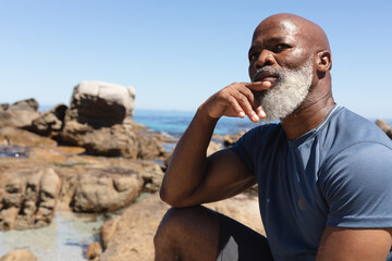 Fit senior african american man sitting on rocky coast thinking