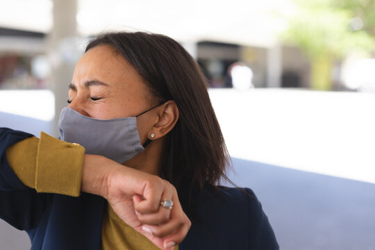 African american woman wearing face mask sneezing on her hand on the street