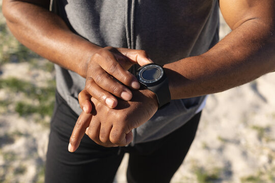 Mid section of fit african american man exercising checking smartwatch