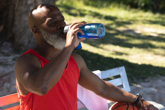 Fit senior african american man sitting in park drinking from water bottle