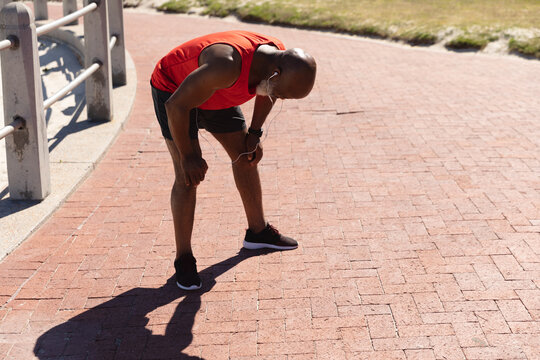 Fit Senior African American Man Wearing Earphones Exercising In The Sun Catching His Breath