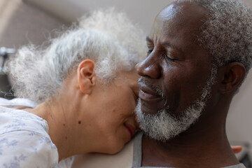 Senior mixed race couple in bedroom sitting on bed embracing