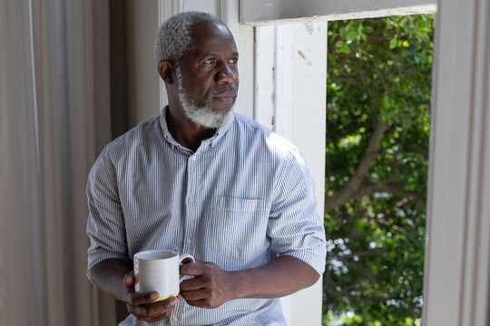 Senior african american man standing by window drinking coffee at home