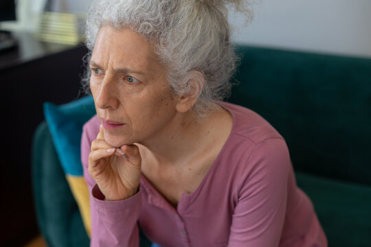 Senior caucasian woman sitting on couch rubbing her chin
