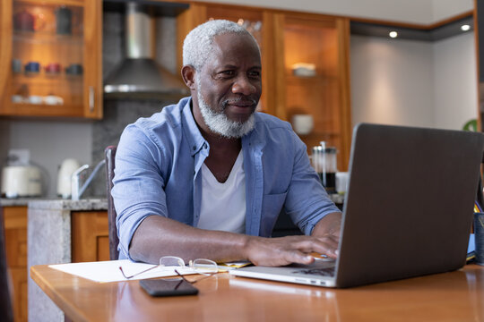 Senior african american man using laptop paying bills in dining room