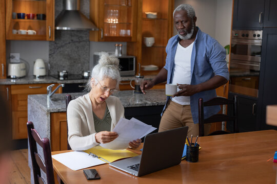 Senior mixed race couple using laptop paying bills together in dining room