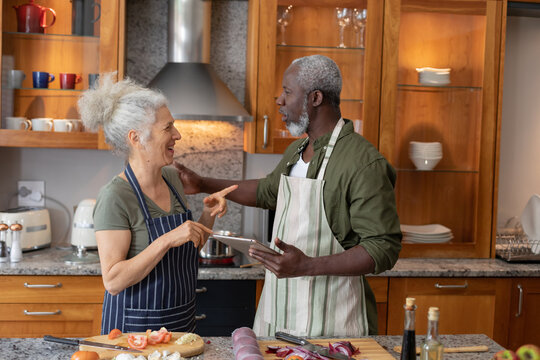 Senior mixed race couple standing in kitchen cutting vegetables