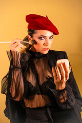 Sexy young female in a red barret hat and a black transparent shirt doing makeup
