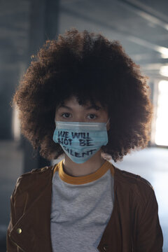 Mixed race woman wearing face mask with slogan looking at the camera