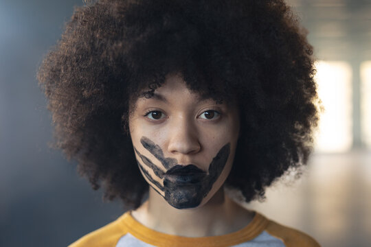 Mixed race woman having a black hand print painted on face looking at camera