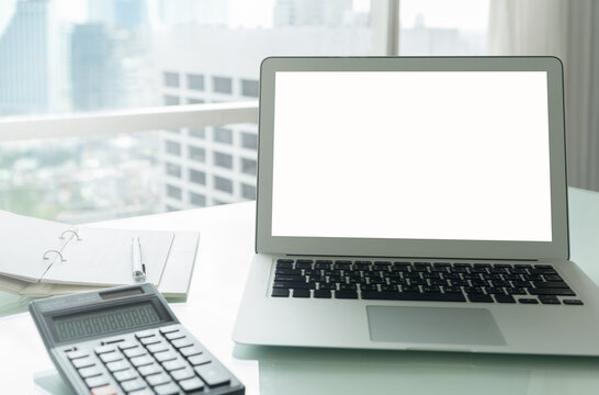 blank white screen laptop monitor with calculator on workspace desk in home offfice. business city view.