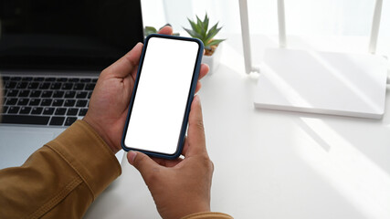 Closeup view of man using smart phone and sitting in front of wireless router at home office.