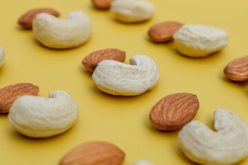 Selective focus closeup of almond and cashew nuts on a mustard color background