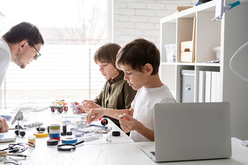 Obraz na płótnie Canvas Young boys and teacher having fun constructing robot cars at the workshop
