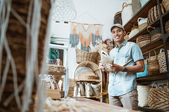 young entrepreneur smiles while holding a wicker wallet while standing in a craft shop