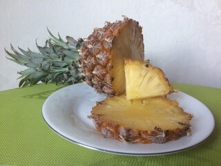 Sliced pineapple lies on white plate on green napkin. Pineapple is one of the most amazing plants, it is herb, namely tropical fruit. This exotic fruit is rich in vitamins and minerals.
