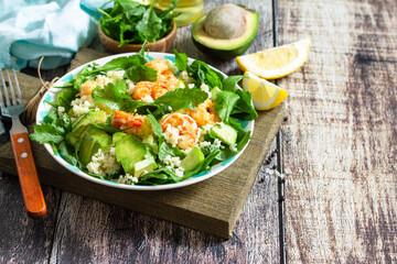 Food dieting concept. Couscous salad with arugula, avocado and grilled shrimps on rustic wooden table. Copy space.