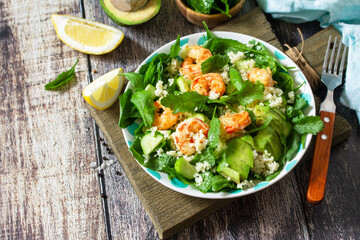 Food dieting concept. Couscous salad with arugula, avocado and grilled shrimps on rustic wooden table. Copy space.