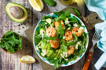 Food dieting concept. Couscous salad with arugula, avocado and grilled shrimps on rustic wooden table. Top view flat lay.