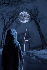 A witch with a stick walks down a narrow street on a winter night. A big full moon shines through...