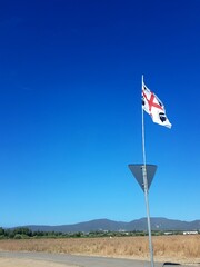 Fototapeta premium The Sardinian flag with the red cross and the four moorishes flies on a road sign in the hinterland of the island