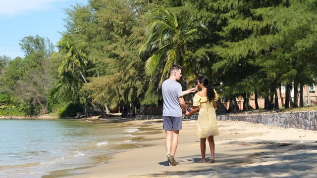 Romantic interracial couple holding hands and walking on beach on a sunny day.
