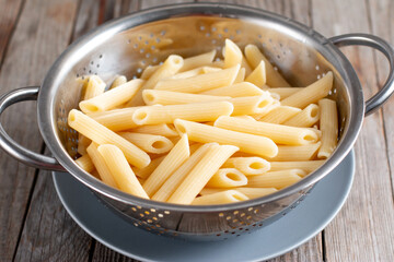 Fresh cooked Penne pasta in colander on table