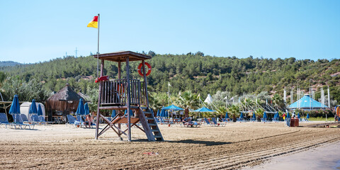 Fototapeta premium Wooden lifeguard tower with red and yellow flag on top stands on sandy beach
