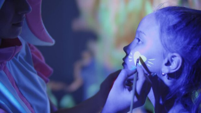 Animator draws neon heart using make up on girl's cheek