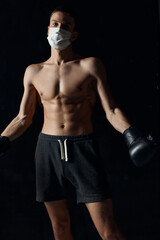 Fototapeta na wymiar sporty man in medical mask and in boxing gloves on black background 