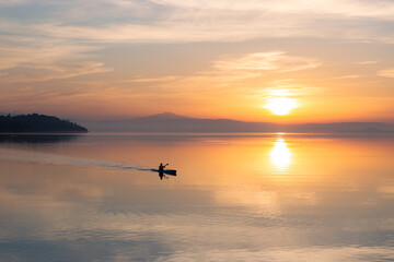 Beautiful sunset at Trasimeno lake with a man on a canoe above perfectly still water