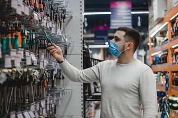 Young man wearing disposable medical mask chooses a screwdriver in the tool shop