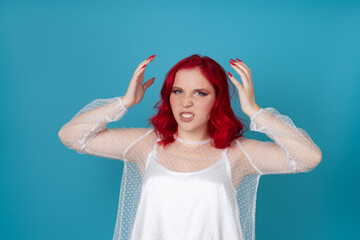 a frustrated, angry woman in a white silk dress and with red hair clutches her head with her hands...
