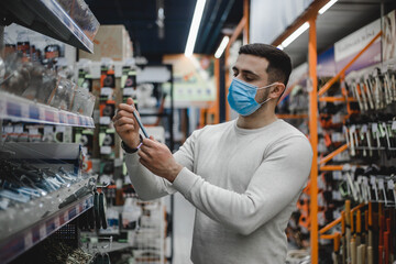 Man in mask standing near the counter and choosing fasteners, screws, nails