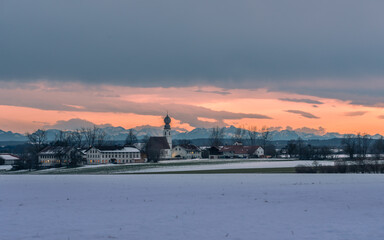 Kirch mit Gebäuden  vor Alpenpanorama bei Sonnenuntergang im Chiemgau im Winter mit Schnee und...