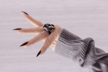 Female hand with long nails and gray black manicure with bottles of nail polish