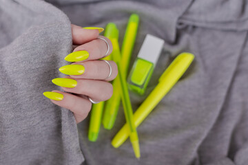 Female hand with long nails and a bottle of bright neon yellow nail polish