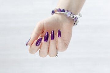 Female hand with long nails and a bottle with purple nail polish