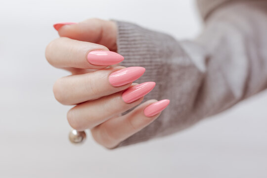Female hand with long nails and a bottle of bright pink neon nail polish