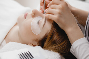 Obraz na płótnie Canvas Eyelash extension procedure. Master tweezers fake long lashes beautiful female eyes