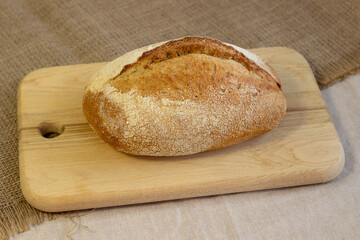 Appetizing freshly baked bread with a golden brown crust on wood cutting board a rough linen cloth close-up