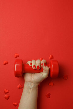 Woman's hand with red dumbbell on red hearts background with copyspace. Valentine's Day fitness composition.