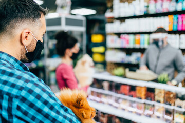 Customers with protective face masks buying accessories and food for their pets in pet shop.