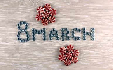 The inscription 8 March from metal nuts with sweets on a wooden background. International Women's Day