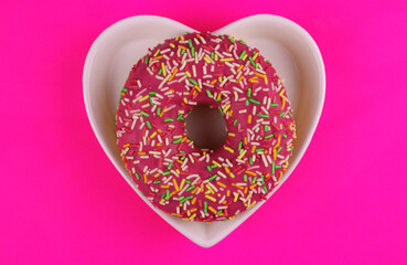 Round sweet pink donut in heart shaped plate on pink background